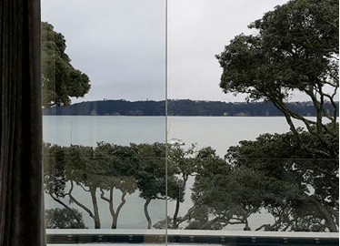 View through glass doors to a balcony with glass balustrades overlooking the sea. Glass balustrades New Plymouth.